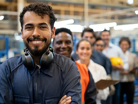 Cheerful handsome blue collar worker and team of engineers at a factory standing in a row smiling at camera with arms crossed